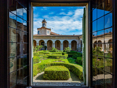 Giardino dei Semplici courtyard from a historical window in Ducal Palace, featuring ancient Italian architecture with arches, columns, and a manicured Renaissance garden under a blue sky