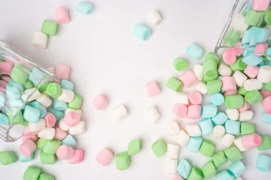 Small pastel colored marshmallows in pink, green, blue, and white cascade from two clear glass containers