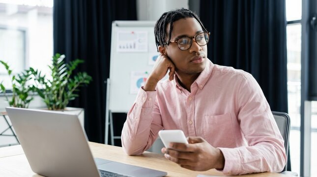 A focused young African American man distracted from his work at a stylish workspace.