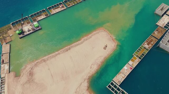 Aerial view showing a bulldozer working on a land reclamation project, expanding the coastline with sand and constructing a concrete caisson breakwater for a new harbor or marina development