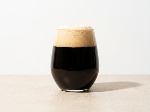 Glass of dark stout beer with thick creamy foam head on table