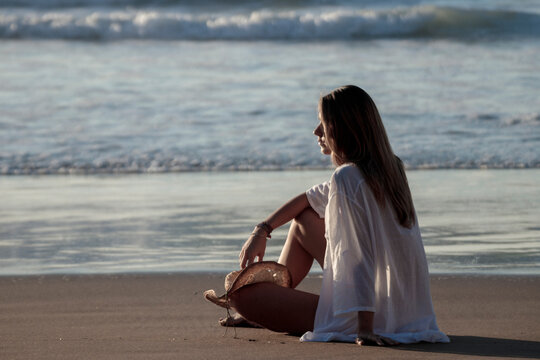 Woman relaxing peacefully on beach watching ocean waves