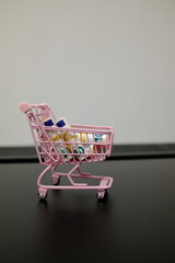 Rolled 10 euro banknotes in pink toy shopping cart on dark surface with copy space © Stanislava