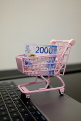 2000 Russian ruble banknote in pink toy shopping cart on open laptop, online shopping and e-commerce concept © Stanislava