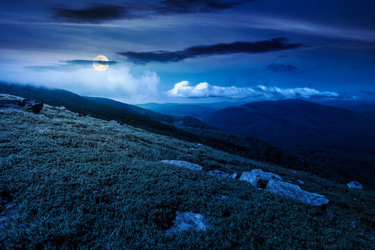 nature scenery with mountain under summer sky at night. full moon over alpine landscape of carpathian mountain with grassy slopes. low fluffy clouds on high altitude. mysterious summer vacations