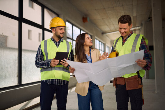 Happy workers and project manager examining blueprints at construction site.