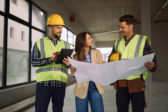 Happy workers and project manager examining blueprints at construction site.