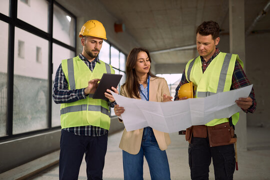 Manual workers and their building contractor cooperating while reading plans at construction site