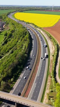Aerial vertical landscape view with downwards motion of a busy UK motorway with speeding traffic through countryside and farmland