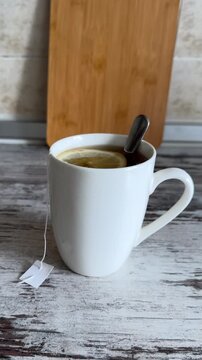 A white ceramic mug filled with hot tea, a tea bag string, a spoon, and a fresh lemon slice floating inside.