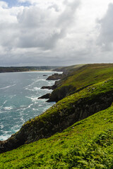 Coastline in Brittany, France. Green hills slope down to rocky shores. Waves crash against cliffs under cloudy sky. No people visible. Ideal for travel, nature, or coastal themes © Дмитрий Маршков