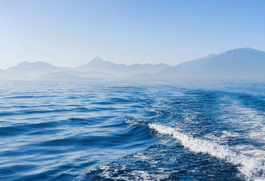 Serene Ocean Landscape with Gentle Waves and Distant Mountain Ranges under Clear Blue Sky for Nature Photography and Travel Backgrounds