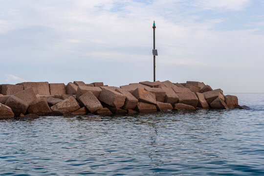 Green navigation beacon on concrete breakwater blocks guarding calm sea waters at Portorosa marina entrance in Tonnarella, Sicily, Italy