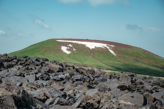 Panoramic Landscape of Volcanic Plateau with Red Earth Cone, Patchy Snow, and Fluffy Cumulus Clouds