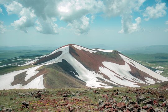 Panoramic Landscape of Volcanic Plateau with Red Earth Cone, Patchy Snow, and Fluffy Cumulus Clouds
