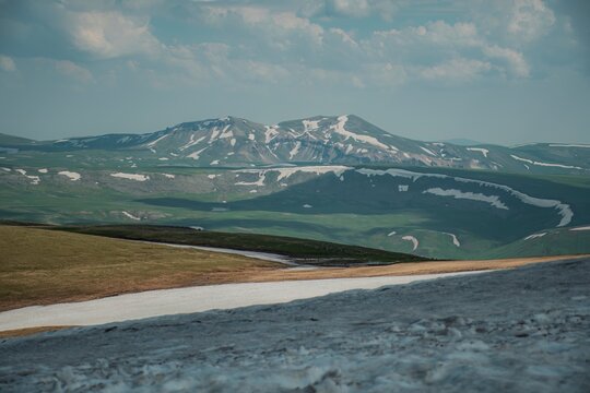 Panoramic Landscape of Volcanic Plateau with Red Earth Cone, Patchy Snow, and Fluffy Cumulus Clouds