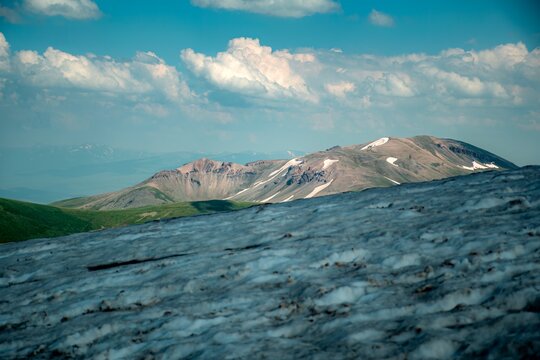 Panoramic Landscape of Volcanic Plateau with Red Earth Cone, Patchy Snow, and Fluffy Cumulus Clouds