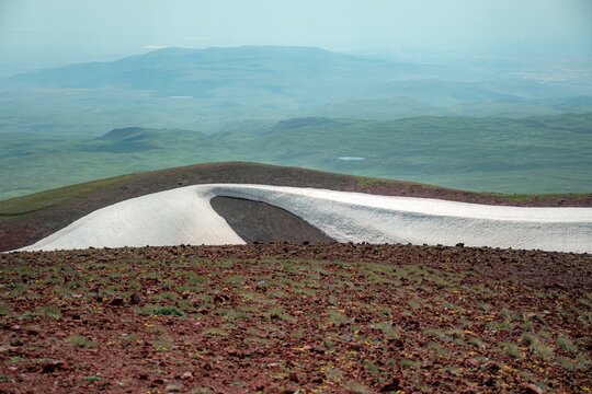 Panoramic Landscape of Volcanic Plateau with Red Earth Cone, Patchy Snow, and Fluffy Cumulus Clouds