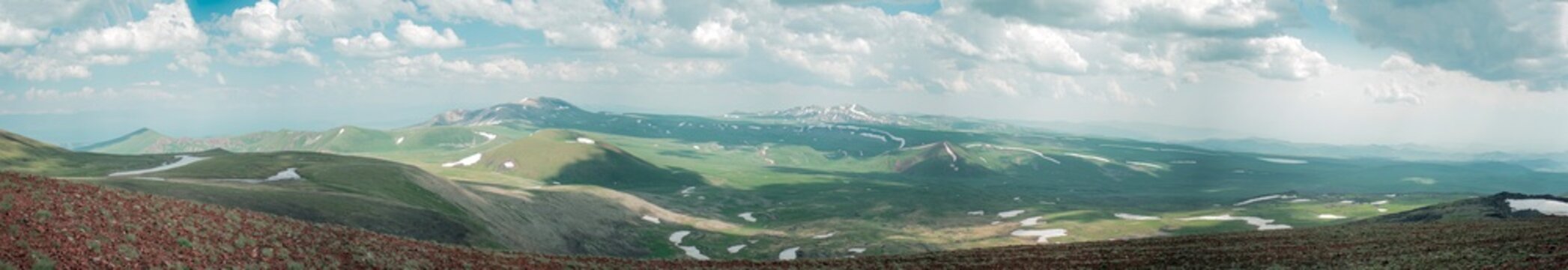 Panoramic Landscape of Volcanic Plateau with Red Earth Cone, Patchy Snow, and Fluffy Cumulus Clouds