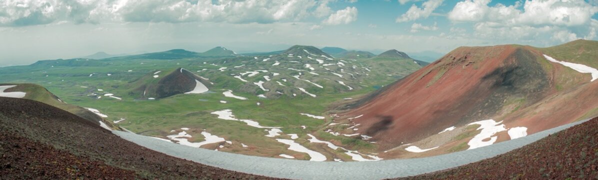 Panoramic Landscape of Volcanic Plateau with Red Earth Cone, Patchy Snow, and Fluffy Cumulus Clouds