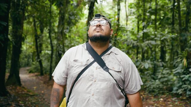Young Latino man looking up at the rainforest canopy while hiking in Arenal Volcano National Park, Costa Rica. Beautiful ecotourism experience