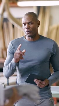 Confident african american male carpenter talking to his team while holding a digital tablet. Mature craftsman giving instructions in a factory
