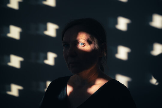 Portrait of a woman partially illuminated by patterned sunlight and shadow.