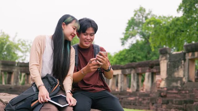 Smiling Asian tourists reviewing map on phone at archaeological park