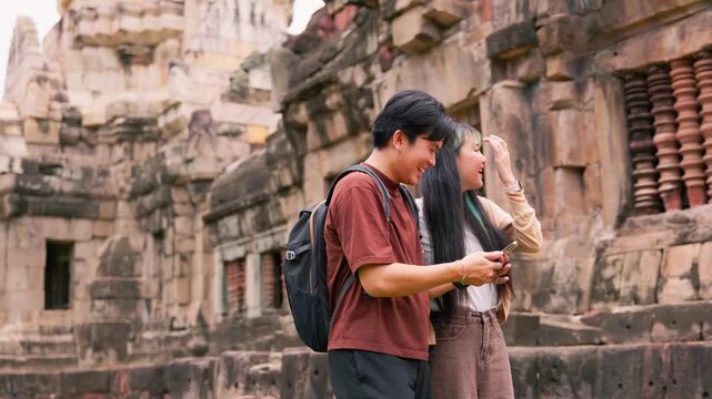 Young Asian backpackers walking and exploring historical stone temple site on sunny day. Travel destination adventure, historic archaeology discovery and summer vacation trip.