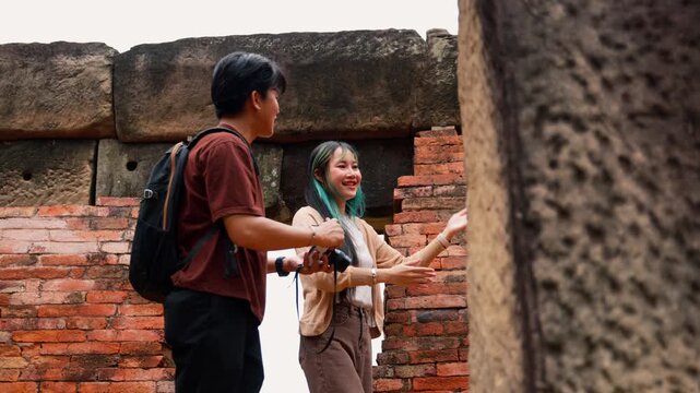 Young Asian backpackers walking and exploring historical stone temple site on sunny day. Travel destination adventure, historic archaeology discovery and summer vacation trip.