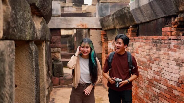 Young Asian backpackers walking and exploring historical stone temple site on sunny day. Travel destination adventure, historic archaeology discovery and summer vacation trip.