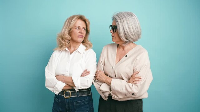 Unhappy senior women standing with arms crossed, showing faces of disgust and dissatisfaction. Studio shot capturing their grumpy mood
