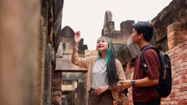 Young Asian backpackers walking and exploring historical stone temple site on sunny day. Travel destination adventure, historic archaeology discovery and summer vacation trip.