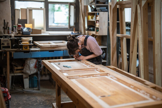Woman craftsmanship in carpentry and restoration, focused female master repairing door in workshop, skilled craftswoman precisely working on details of wooden door with chisel, remaking process.