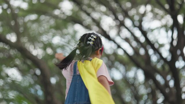 Cute Asian children playing superhero roleplay with colorful cape and mask running in outdoor green park. Kids imagination, creative future dream, and brave hero inspiration.