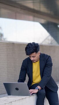 Stylish Moroccan businessman sitting outdoors and typing on his laptop. A focused male entrepreneur working remotely on a project. Vertical