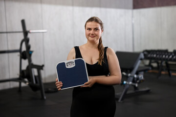 Fototapeta premium Happy overweight woman with scales in gym