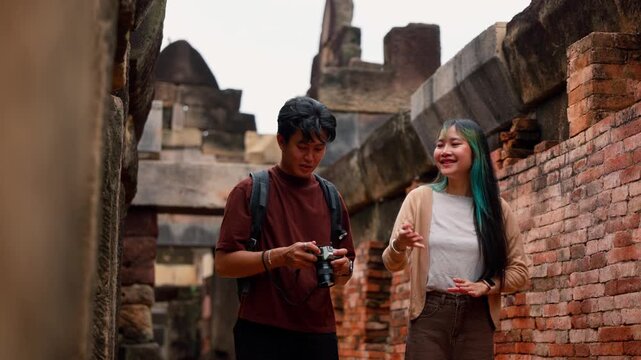 Young Asian couple vloggers recording video and taking photos at historical stone temple ruins. Travel destination adventure, historic archaeology discovery and summer trip.