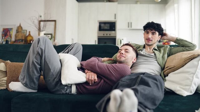 Affectionate male couple cuddling together on the couch. Homosexual partners enjoying a quiet, intimate moment at home in the living room