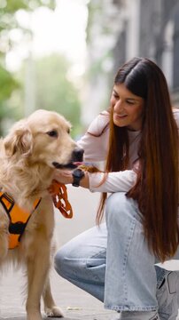 Young smiling woman affectionately stroking her beautiful golden retriever during a walk. Loving pet owner enjoying a moment with her canine friend