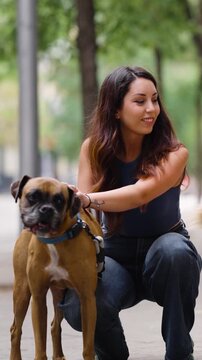 Happy young woman crouching on the sidewalk and petting her adorable brown boxer dog. A beautiful moment of love between a pet and its owner