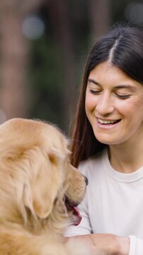 Young smiling woman having fun with her golden retriever. Close up of the dog licking its owner's face with love in a beautiful park