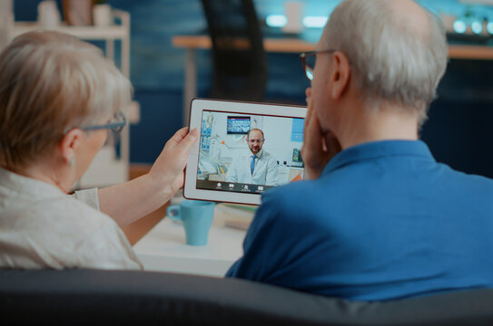 Senior patients with toothache call a dentist on a digital tablet, using remote video consultation to discuss dental care and healthcare advice at home.