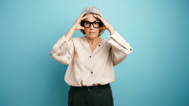 Senior woman with grey hair feeling distressed and anxious, holding her head, dealing with a headache or serious problem