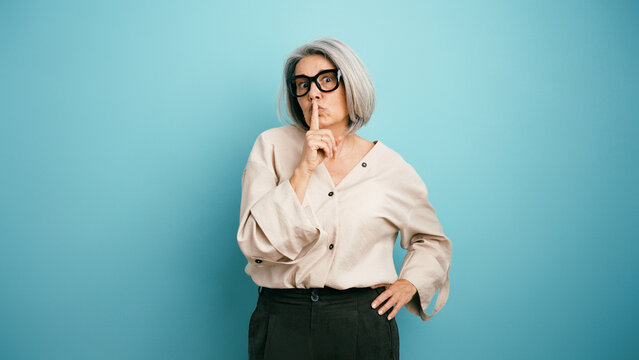 Mature woman making a shhh gesture with finger on lips, asking for quiet, keeping a secret, expressing confidentiality