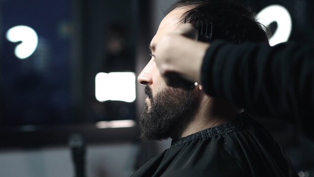 Professional barber trimming client's hair using electric clipper, creating stylish fade for bearded man in modern barbershop setting