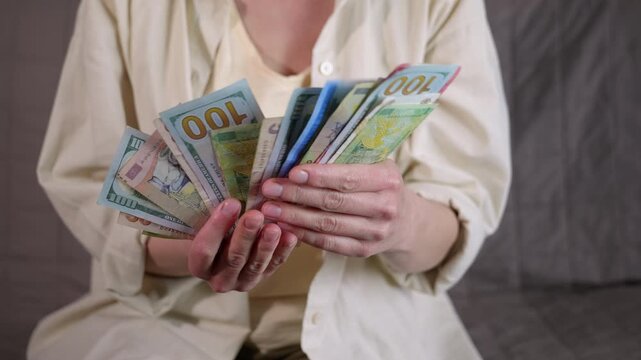 Woman holding various currencies in her hands. Anonymous woman sitting and holding a fan of mixed paper banknotes from different countries, including us dollars, showcasing international finance