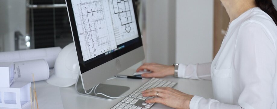 Architect woman working on blueprints and building plans using computer aided design in modern office. Business and architecture concept