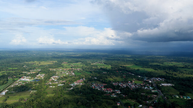 La Fortuna town nestled in dense rainforest and agricultural fields beneath an impressive sky with a mix of sun and clouds