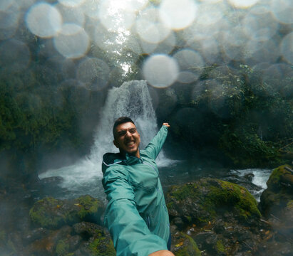 Man smiling, pointing to a tropical waterfall in Costa Rica's lush rainforest. Adventure and travel concept